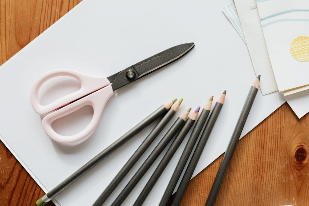 Top view of a creative workspace featuring scissors and colored pencils on a wooden table.